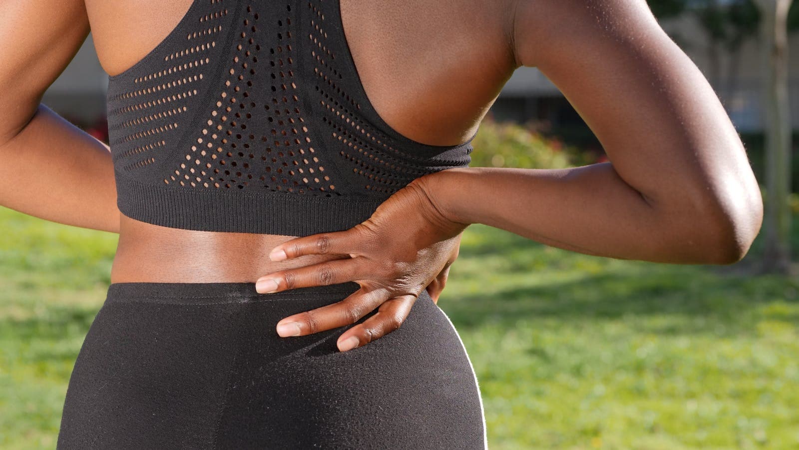 Mulher com a mão apoiada na região lombar indicando desconforto em ambiente externo